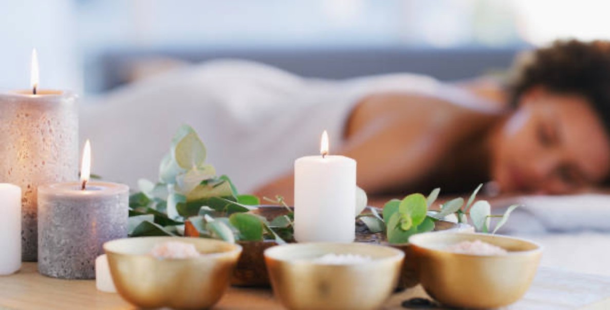 Relaxing spa scene with candles and bowls in the foreground and a person resting in the background.